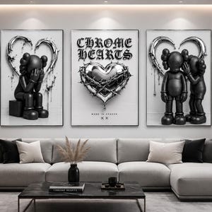 May include: A set of three wall art prints featuring black cartoon figures and a metallic heart. The left print shows a figure sitting, the center displays a heart with barbed wire and the text CHROME HEARTS, and the right shows two figures.