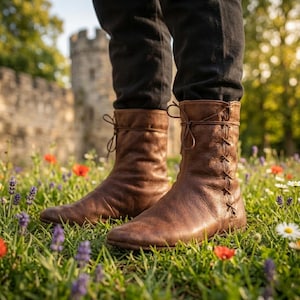 Peut inclure: Une paire de bottes mi-mollet en cuir marron dotées d'un laçage latéral avec de fines cordes en cuir nouées sur le dessus. Les bottes présentent un bout arrondi, une texture lisse et sont portées avec un pantalon noir, montrant une structure simple.
