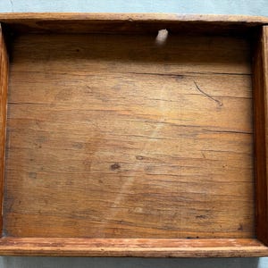 May include: A rectangular wooden tray with a natural brown finish, featuring visible wood grain, horizontal planks, and raised edges on all four sides. The surface shows signs of wear with subtle scratches and variations in the wood tone.