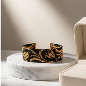 May include: A wide cuff bracelet crafted from tiny black and gold beads, featuring a repeating floral pattern of golden tulips against a solid black background. The bracelet is finished with metallic gold end caps on both sides of the band.