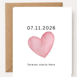 May include: A white greeting card featuring a watercolor-style pink heart in the center. Above the heart, the date 07.11.2026 is printed in black text. Below the heart, the phrase forever starts here is printed in black, lowercase text.