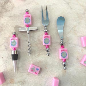 May include: A collection of bar tools and mahjong tiles. The tools include a corkscrew, fork, and spreader, each with a pink tile that says "JOKER". The tiles are pink with blue and green symbols.