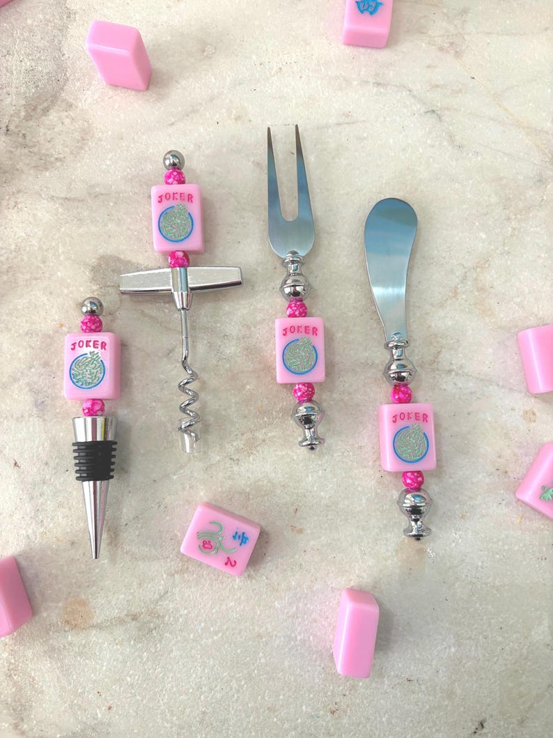 May include: A collection of bar tools and mahjong tiles. The tools include a corkscrew, fork, and spreader, each with a pink tile that says "JOKER". The tiles are pink with blue and green symbols.
