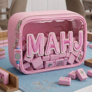 May include: A pink zippered case with a clear front panel, filled with pink Mahjong tiles. The word "MAHJ" is embroidered in pink on the clear panel. A "JOKER" charm hangs from the zipper. The tiles are arranged on a light blue surface.