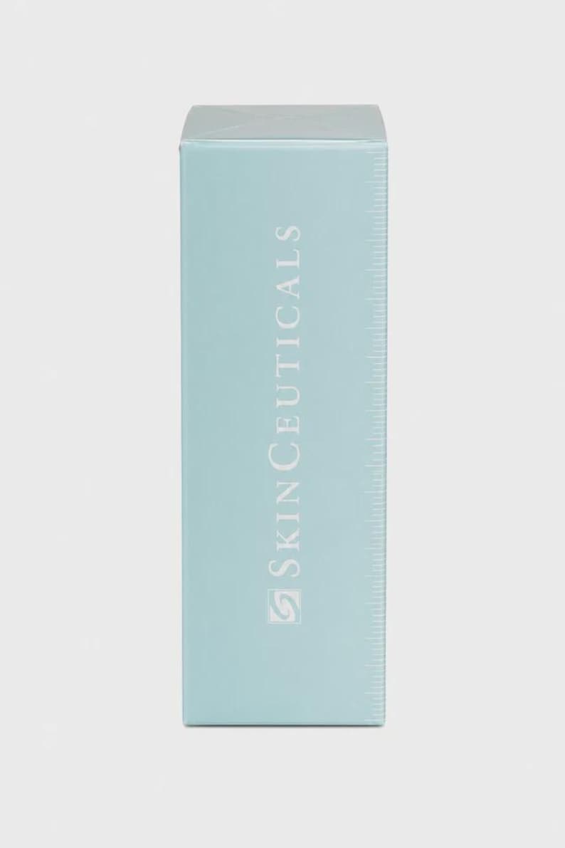 Op de afbeelding: Een lichtblauwe rechthoekige doos met de witte tekst "SkinCeuticals". De doos heeft een liniaalachtig ontwerp aan de rechterkant. De productverpakking is effen lichtblauw.