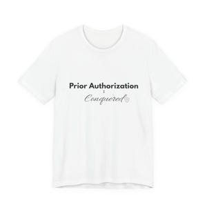以下が含まれることがあります： 「Prior Authorization: Conquered」の黒い文字がプリントされた白いTシャツ。上のテキストは太字のサンセリフ体で、下のテキストは小さなハートのシンボルが付いた筆記体です。