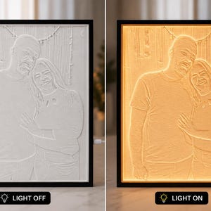 Puede incluir: Una pieza de arte mural rectangular enmarcada que presenta un retrato en relieve 3D de dos personas de pie una al lado de la otra. La obra se muestra en dos estados: apagada en blanco y encendida con una cálida luz de color ámbar.