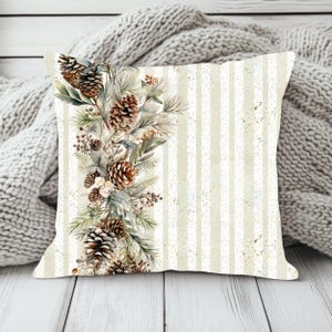 May include: A square throw pillow featuring a vertical arrangement of pinecones, evergreen needles, and small berries on the left side. The background consists of alternating cream and white vertical stripes with a subtle speckled texture throughout.