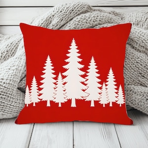 May include: A square throw pillow featuring a vibrant red background with a repeating pattern of white pine trees in varying heights. The trees are arranged in a row across the center of the pillow, creating a stark contrast against the solid red color.