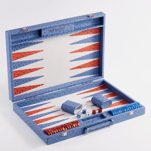 May include: Blue backgammon set with red and white triangular patterns. The set includes dice, dice cups, and game pieces. The set is embossed with a textured pattern and the text "ELIE RAPHAEL".
