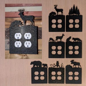 May include: A collection of black glittery electrical outlet covers featuring various wildlife silhouettes including deer, bears, foxes, owls, and moose. Each square plate is designed for a double duplex outlet with four circular openings.