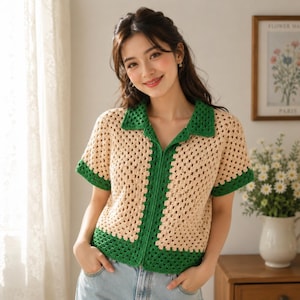 Op de afbeelding: Een gehaakt shirt met korte mouwen in een beige granny square patroon, voorzien van een effen groene kraag, groene mouwboorden en een groene onderzoom. Het kledingstuk heeft een knoopsluiting aan de voorzijde en een klassiek kraagontwerp.