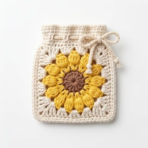 Puede incluir: Una bolsa cuadrada de ganchillo con un motivo central de girasol con un centro marrón oscuro y pétalos de color amarillo brillante. El borde es de hilo color blanco roto y la parte superior incluye un cierre de cordón con un lazo a juego.