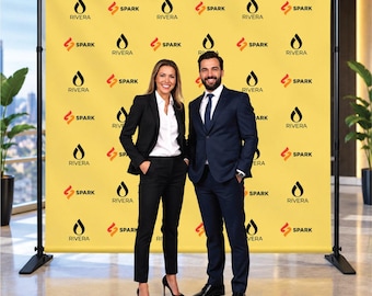 May include: A large yellow step and repeat banner featuring a repeating pattern of the black Rivera logo and the orange Spark logo. The banner is mounted on a black metal stand with adjustable poles and a wide base, designed for event backdrops.