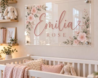 May include: A rectangular clear acrylic wall sign featuring the name Emilia Rose in pink script and block lettering, decorated with pink floral illustrations and green leaves, mounted with four silver metal standoffs at the corners.