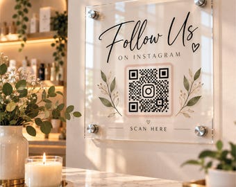 May include: A clear acrylic square sign mounted with four silver standoffs. The sign features black text reading Follow Us ON INSTAGRAM, a central QR code with an Instagram icon, green leaf illustrations, and the text SCAN HERE at the bottom.