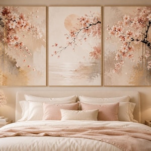 以下が含まれることがあります： 桜の枝が描かれた穏やかな風景の、額装されたアートプリントの三連作。ベージュ、ピンク、ブラウンの柔らかな色使い。お揃いの装飾が施されたベッドの上に飾られています。