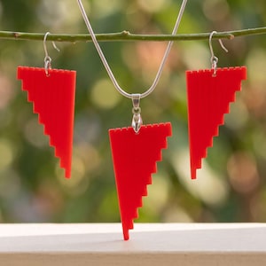 Op de afbeelding: Een sieradenset bestaande uit een zilverkleurige slangenketting met een rode, getrapte, driehoekige hanger en twee bijpassende rode, getrapte, driehoekige oorbellen met zilverkleurige metalen haken en een gekartelde rand.
