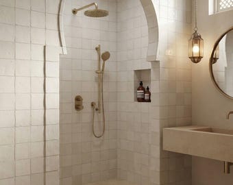 May include: A bathroom featuring a walk-in shower enclosed by a Moorish archway, lined with off-white square tiles. The shower includes brass fixtures, a rainfall showerhead, and a handheld sprayer. A stone sink and a round mirror are nearby.