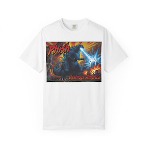 May include: White t-shirt featuring a graphic of Godzilla breathing blue fire, with the text "Phish Destroys America." The design is set against a backdrop of a city in flames. The shirt has a crew neck.
