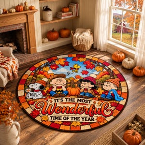 Puede incluir: Una alfombra redonda con una escena otoñal de Peanuts que muestra a Snoopy, Charlie Brown, Lucy y Linus rodeados de hojas de otoño y calabazas. El texto dice "IT'S THE MOST Wonderful TIME OF THE YEAR" en letras naranjas y rojas.