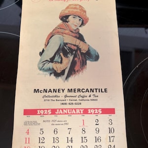 May include: Vintage 1925 January calendar from Liberty magazine, featuring an illustration of a woman in a hat and scarf. The calendar includes the McNaney Mercantile store information.