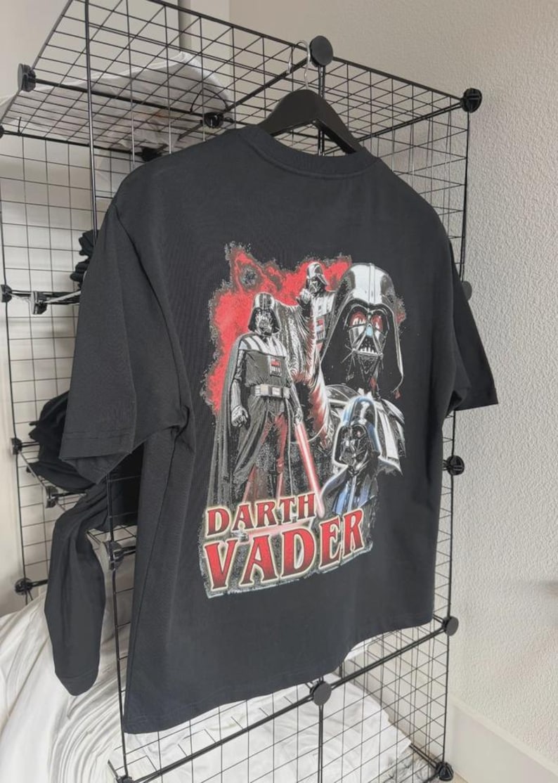 May include: Black t-shirt featuring a graphic of Darth Vader from Star Wars. The design includes multiple images of Darth Vader with a red and white color scheme. The text "Darth Vader" is printed in red and white.