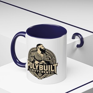 Peut inclure: Un mug en céramique blanche avec un intérieur et une anse bleu foncé. L'avant présente un graphique d'une personne musclée avec des tatouages traditionnels dans un emblème circulaire, avec le texte POLYBUILT DIFFERENT en lettres capitales noires.
