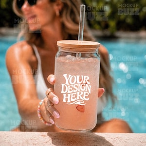 Op de afbeelding: Een doorzichtig glas met een bamboe deksel en een recht glazen rietje, gevuld met een roze drankje met ijsblokjes en een schijfje aardbei. Op de voorkant van het glas staat de witte tekst "YOUR DESIGN HERE" in een gestileerd lettertype.