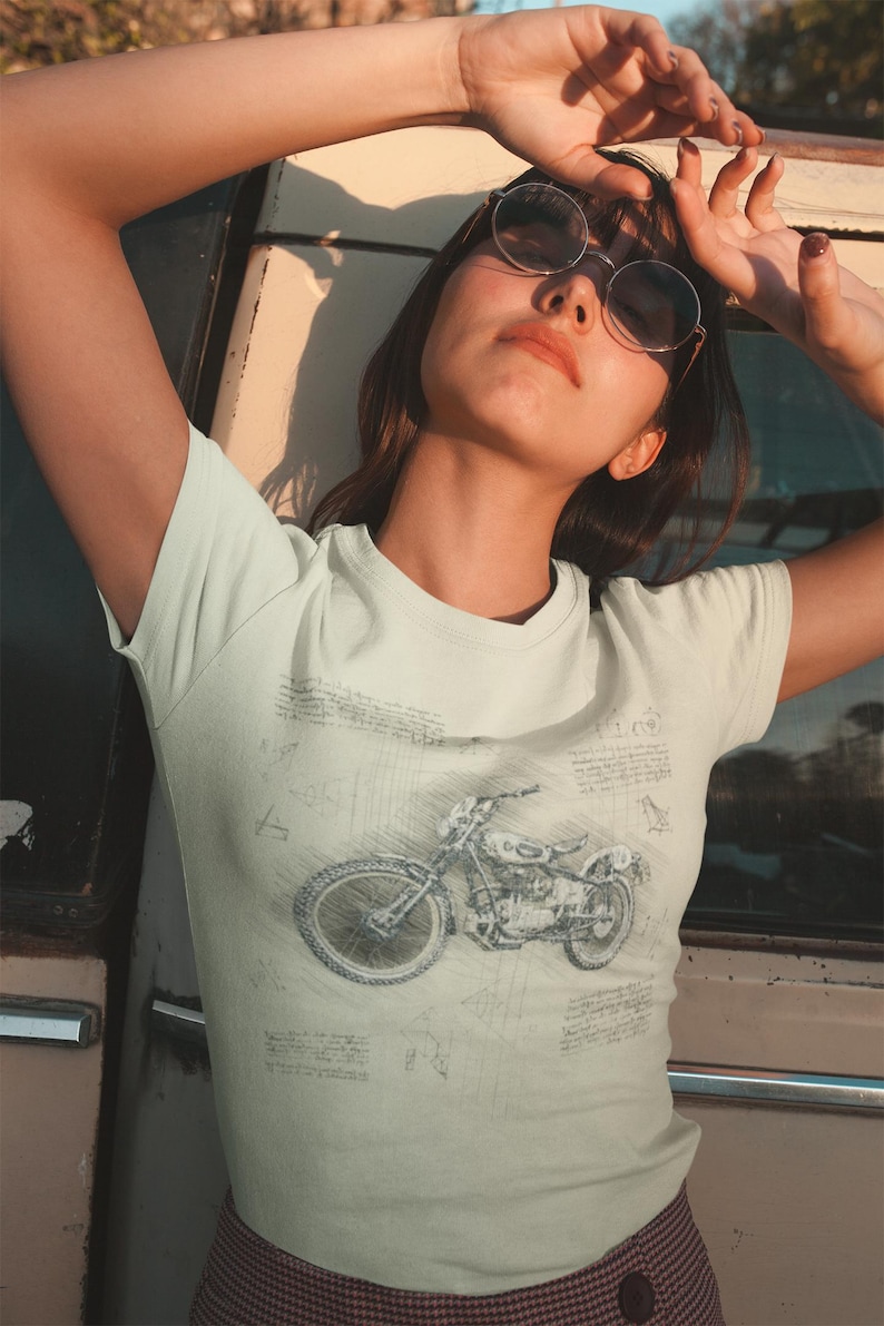 K&ouml;nnte beinhalten: Hellfarbenes T-Shirt mit einer detaillierten Skizze eines Motorrads. Das Design ist im Vintage-Stil gehalten, mit komplizierten Linien und Schattierungen. Das Shirt hat eine helle Farbe, m&ouml;glicherweise cremefarben oder cremefarben.