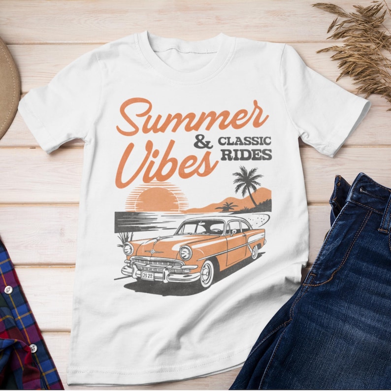 K&ouml;nnte beinhalten: Ein wei&szlig;es Kurzarm-T-Shirt mit einem Grafikdruck eines orangefarbenen Oldtimers, der bei Sonnenuntergang an einem Strand geparkt ist. Der Text Summer Vibes & Classic Rides ist in Orange und Dunkelgrau gehalten, erg&auml;nzt durch eine Palme.