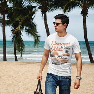 K&ouml;nnte beinhalten: Ein wei&szlig;es kurz&auml;rmeliges T-Shirt mit einem Grafikdruck eines Oldtimers am Strand mit Palmen und dem Text Summer Vibes & Classic Rides in orangefarbener und schwarzer Schrift, kombiniert mit einer blauen Jeans und einer dunklen Sonnenbrille.