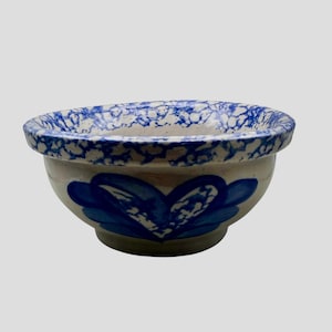 May include: A ceramic bowl featuring a cream-coloured base with a blue sponge-painted rim and a hand-painted blue floral motif on the exterior. The bowl has a rounded shape with a thick, curved edge and a smooth, glossy finish throughout the piece.