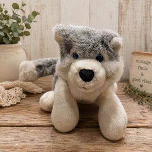 May include: A plush wolf toy featuring soft grey and white fur, pointed ears, and bright blue eyes. The stuffed animal has a black nose and a fluffy tail, designed with a realistic appearance and a friendly expression, crafted from soft fabric.