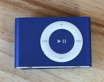 Può includere: Un lettore musicale digitale blu di forma rettangolare con un'interfaccia di controllo circolare bianca sulla parte anteriore. L'interfaccia include un pulsante centrale di riproduzione e pausa, circondato da simboli.