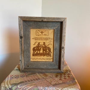 May include: A rectangular wooden frame with a weathered gray finish containing a tan print titled The Code of the West. The print features a graphic of two cowboys on horseback shaking hands, accompanied by text outlining a code of conduct.
