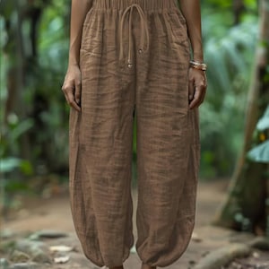 May include: Brown linen pants with a drawstring waist and pockets. The pants have a relaxed fit and a slightly gathered ankle. The fabric appears to be lightweight and breathable, suitable for warm weather. The pants are a solid, earthy brown color.