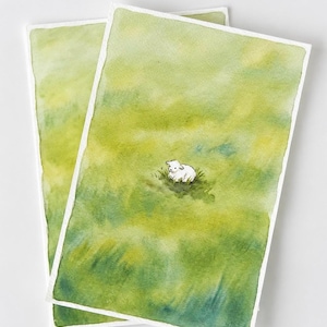 May include: Two rectangular art prints featuring a watercolor painting of a small white lamb resting in a vast, textured field of vibrant green and yellow grass. The artwork uses soft, blended brushstrokes to create a serene, open landscape.