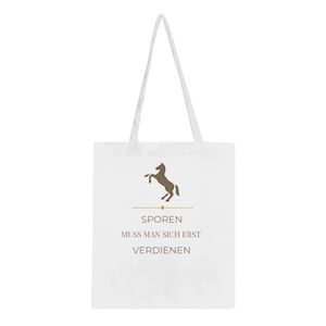 Op de afbeelding: Witte draagtas met lange hengsels. De tas heeft een bruin silhouet van een steigerend paard boven de Duitse tekst "SPOREN MUSS MAN SICH ERST VERDIENEN" in een schreefletter. Het ontwerp is gecentreerd op de voorkant van de tas.
