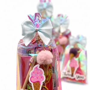 May include: An iridescent plastic gift bag tied with a light blue satin bow. The bag contains a pen, a pink pom-pom ice cream cone keychain, and a sticker featuring an ice cream cone with the text Thank you printed in black script.