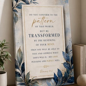 May include: A framed canvas print featuring a scripture from Romans 12:2. The artwork displays the text "Do not conform to the pattern of this world, but be transformed..." in gold lettering. The print is decorated with watercolor-style blue and gold foliage.