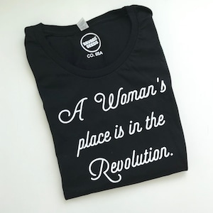 May include: Black t-shirt with white text that reads "A Woman's place is in the Revolution."