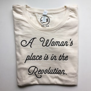 May include: A white t-shirt with the text "A Woman's place is in the Revolution." printed in black.