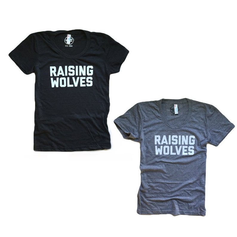 May include: Two t-shirts with the text "Raising Wolves" printed in white on the front. The shirt on the left is black and the shirt on the right is gray.