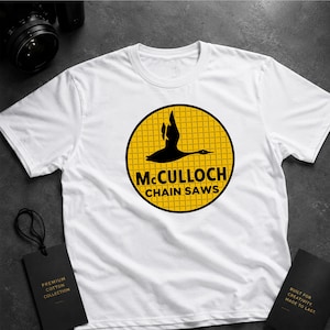 May include: White t-shirt with a yellow circular logo displaying a black goose and the words "McCULLOCH CHAIN SAWS". The tee has a crew neck and short sleeves. Black tags are also visible in the image.