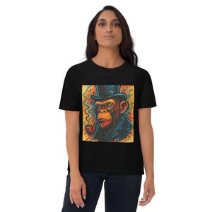 May include: A black t-shirt featuring a square graphic print of a chimpanzee wearing a top hat and a monocle while smoking a pipe. The artwork uses vibrant orange, yellow, blue, and red colors with a painterly, abstract background design.