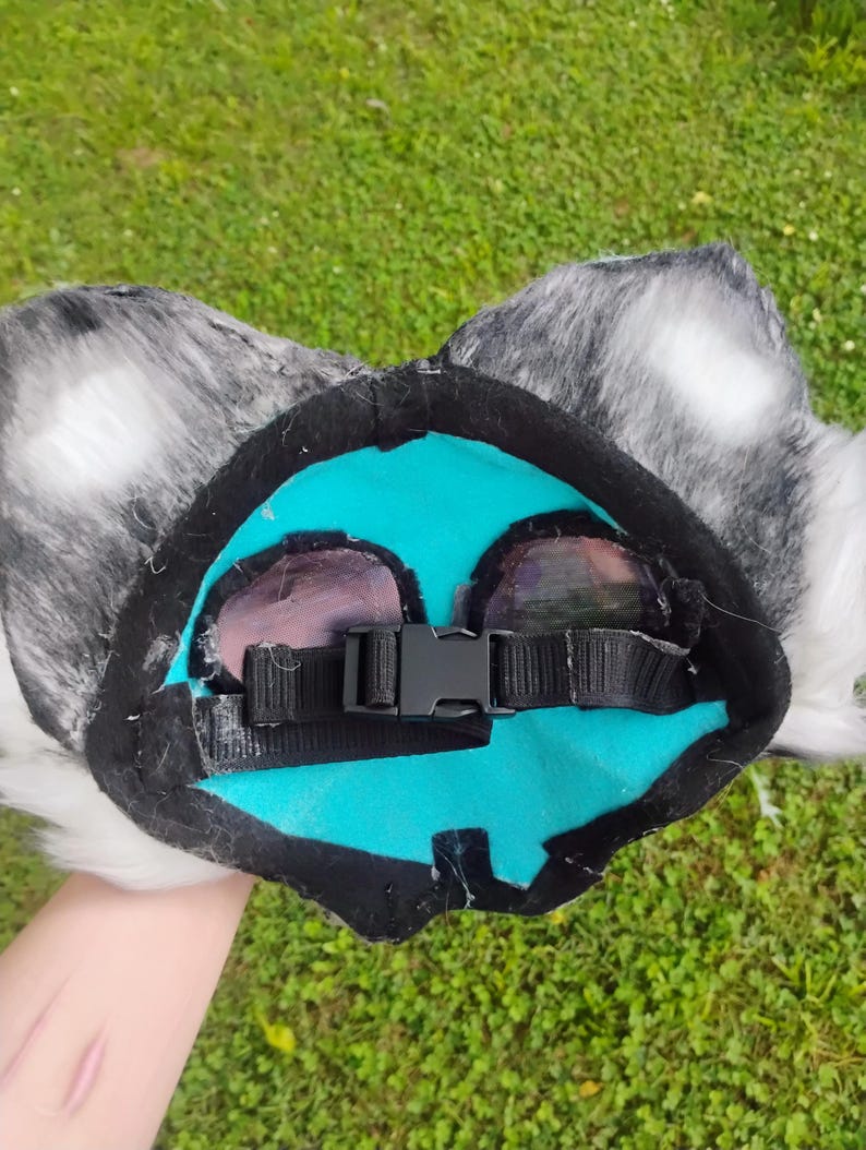 Puede incluir: Una diadema de orejas de animal hecha de piel sint&eacute;tica moteada en gris y blanco. El forro interior es de fieltro turquesa brillante con un borde de tela negra. Una correa de nailon negra ajustable con hebilla de pl&aacute;stico est&aacute; en el centro.