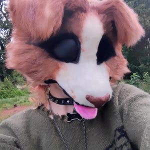Puede incluir: Una m&aacute;scara de animal de piel sint&eacute;tica marr&oacute;n y blanca con grandes cuencas oculares negras, una nariz marr&oacute;n y una lengua rosa sobresaliente. La m&aacute;scara se lleva con un collar negro con tachuelas, una placa en forma de hueso y una cadena.