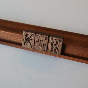 Pu&ograve; includere: Tre tessere rettangolari da mahjong in legno marrone scuro, appoggiate su un supporto in legno. La prima tessera presenta l'illustrazione di un uccello e il numero 1, la seconda mostra tre rettangoli verticali e il numero 3, e la terza mostra nove rettangoli e il numero 9.
