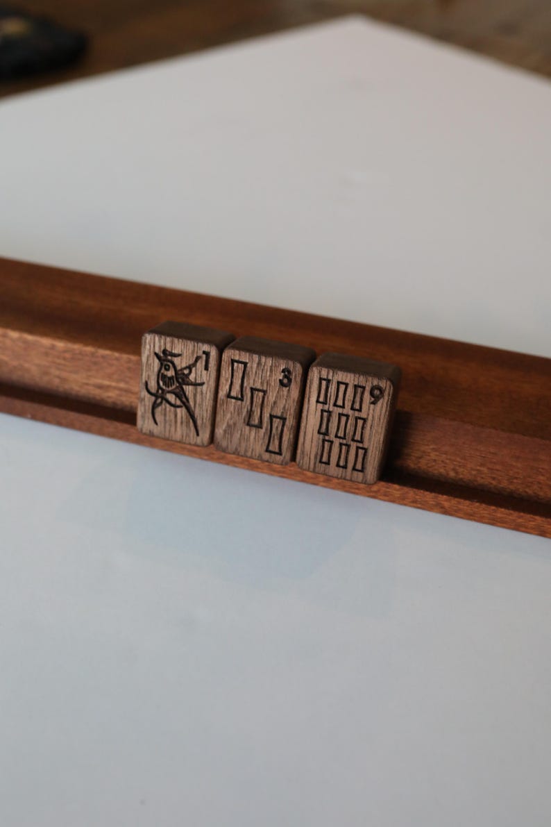 Pu&ograve; includere: Tre tessere rettangolari da mahjong in legno marrone scuro, appoggiate su un supporto in legno. La prima tessera presenta l'illustrazione di un uccello e il numero 1, la seconda mostra tre rettangoli verticali e il numero 3, e la terza mostra nove rettangoli e il numero 9.